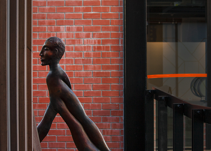 A bronze statue of a man by a red brick wall - color in photography